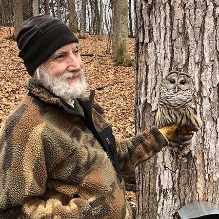 Bearded man holding owl camouflaged against a tree