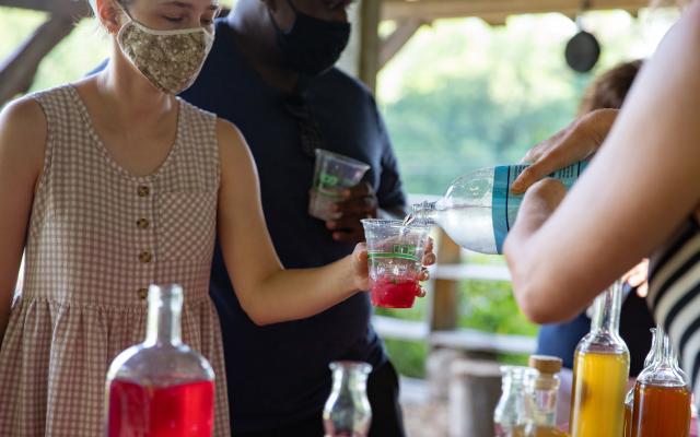 A participant hold out a cup with red syrup and ice, seltzer is poured over top.