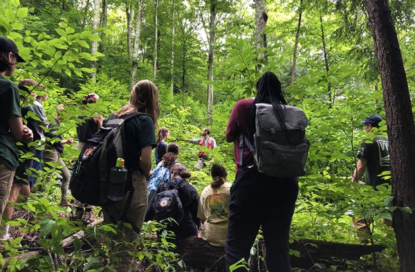 Forestry class of students stand in woods with instructor