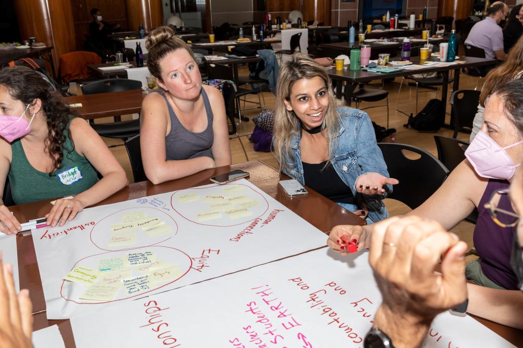 Teachers gather around a table covered in markers and colorful posters at the Coach Barn.