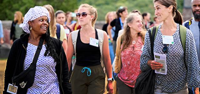 A large group of educators on a walking tour of Shelburne Farms. Two educators at front of group smile at each other in conversation.