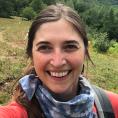 Educator Kat Robbins smiles in a selfie while on a hike. She wears a bandana around her neck and carries a backpack.