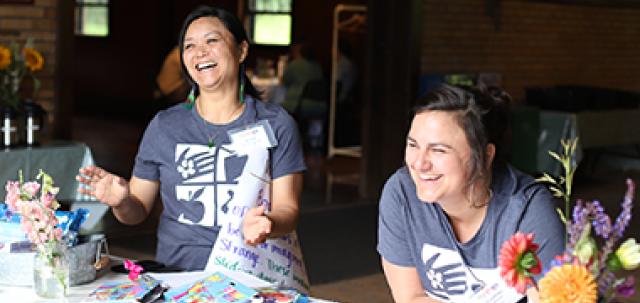 Two educators smile at registration table wearing matching shirts