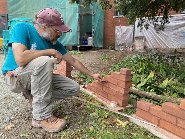 Worker holds up mortar samples agains bricks to test and match new mortar color to historic one.